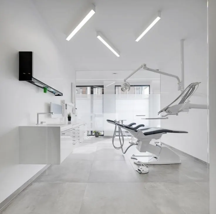 Beyaz ışıklı lineer armatürlerle aydınlatılmış diş kliniği tedavi odası
